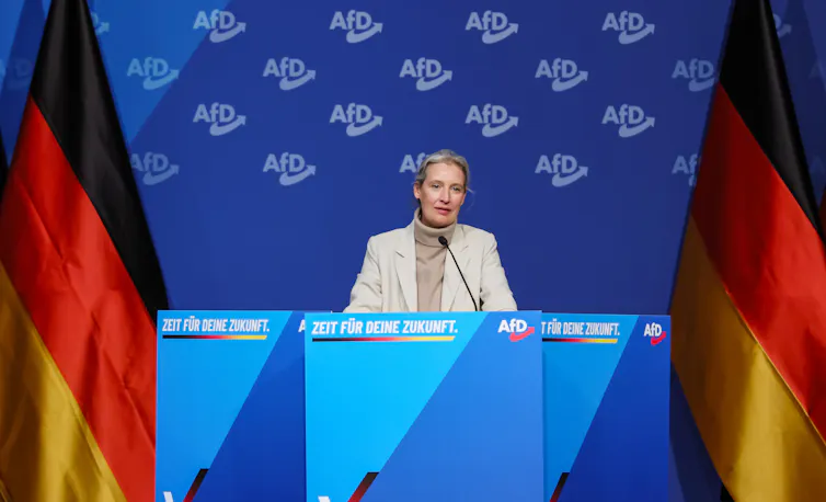Alice Weidel speaks at an event flanked by German national flags.