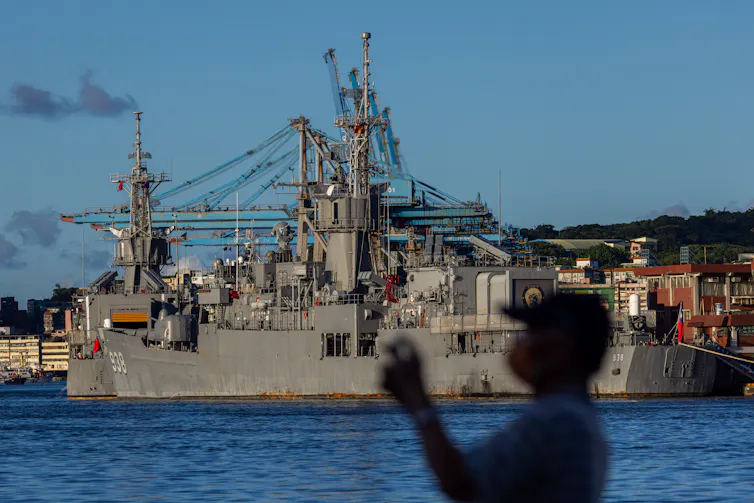 The outline of a man is seen in front of a large ship.
