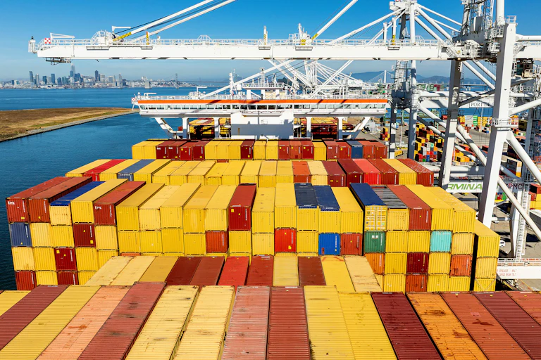 Cargo containers of different colors line a ship at the Port of Oakland, against a blue sea and blue sky, on Aug. 6, 2025, in Oakland, Calif.