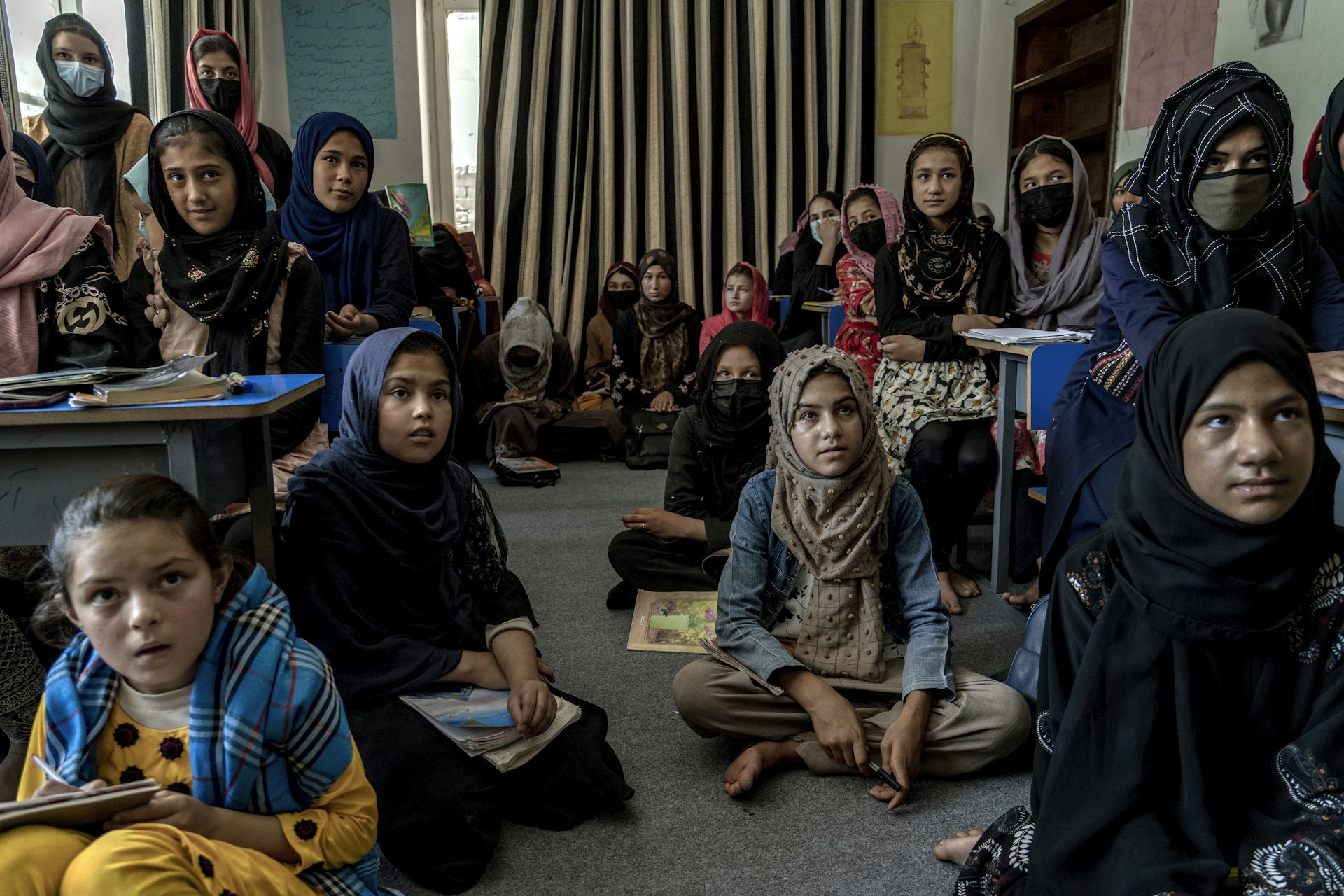 Des filles portant un foulard sont assises dans une salle de classe plongée dans la pénombre.