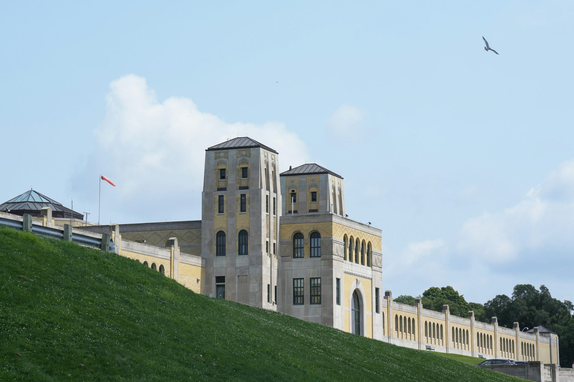 An art deco building by a lake. A bird flies overhead.
