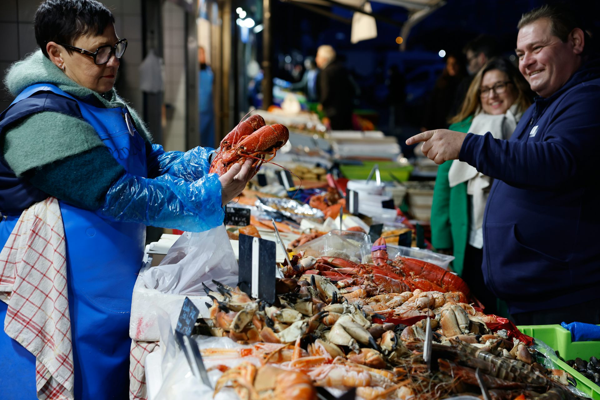 A woman picks up whole lobsters from a market stall.