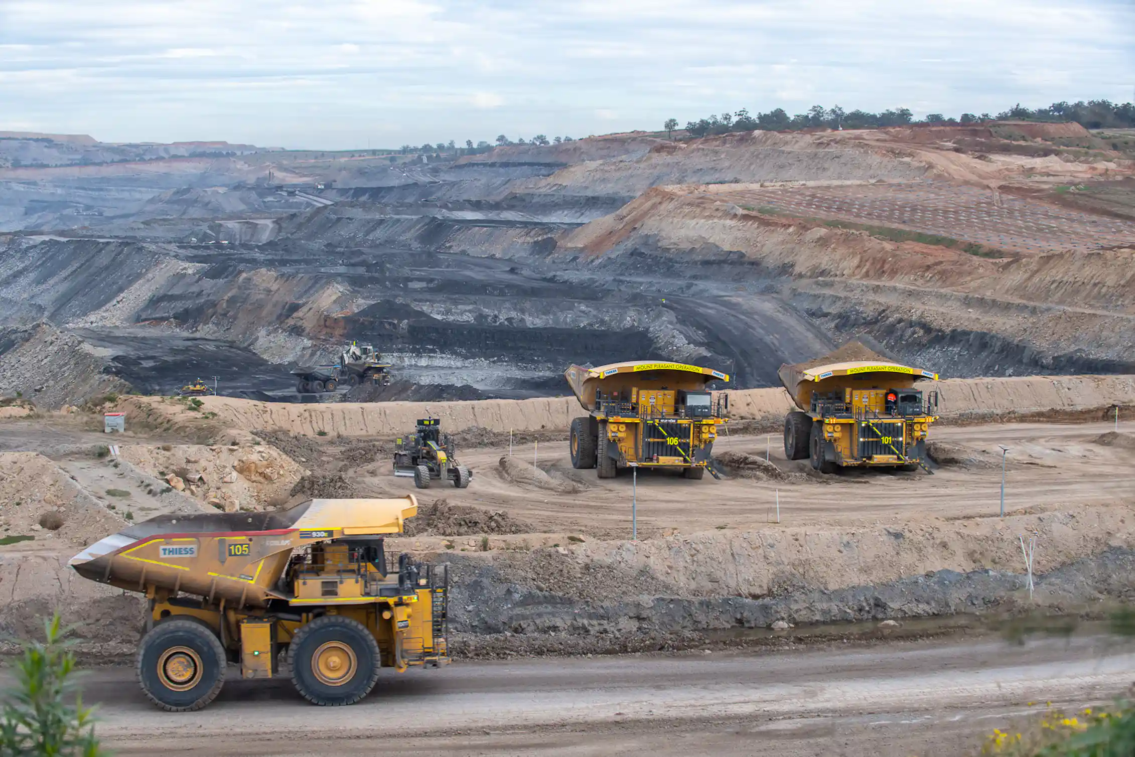 dump trucks in foreground, coal mine behind.