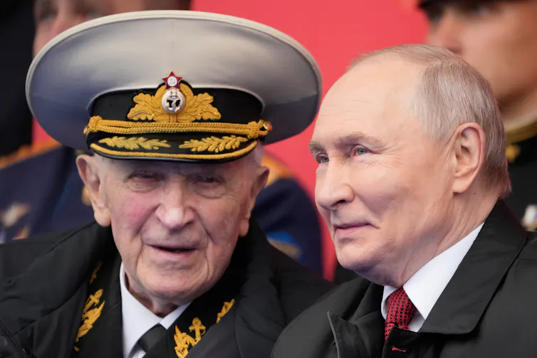 Vladimir Putin speaks with an elderly man in military uniform.