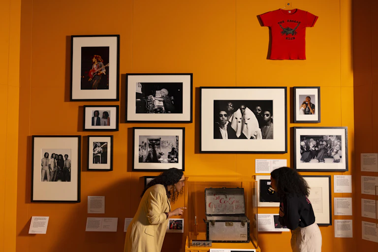 Two women looking at black and white photos hung on an orange wall.