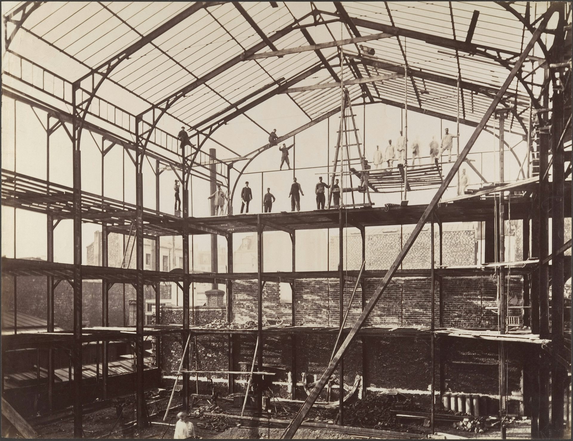 photo en noir et blanc d'un hangar en ver et métal avec des ouvriers en équilibre sur des poutres
