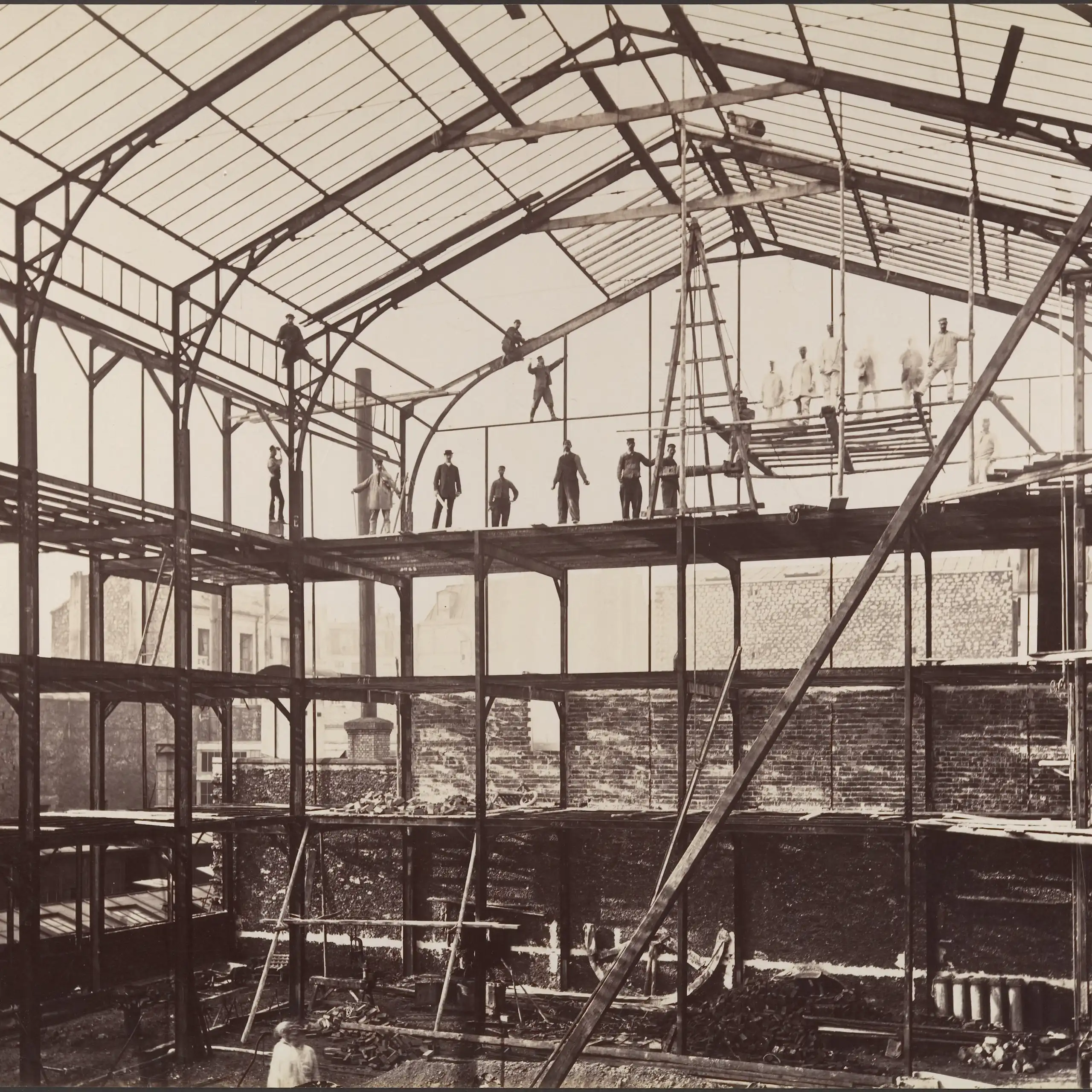photo en noir et blanc d'un hangar en ver et métal avec des ouvriers en équilibre sur des poutres