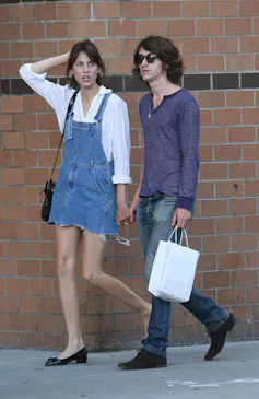 Alexa Chung in a denim pinafore and Alex Turner with long hair, sunglasses and jeans.