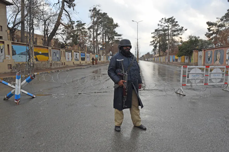 A man in a gun stands in the middle of a street.