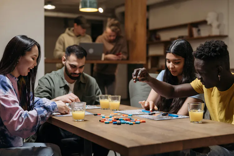 No es sólo un pasatiempo divertido: los juegos de mesa pueden ayudar a construir relaciones y reducir el estrés 1 La gente se sienta en una mesa y juega un juego de mesa.