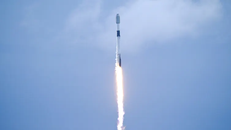 A satellite launches against a blue sky.