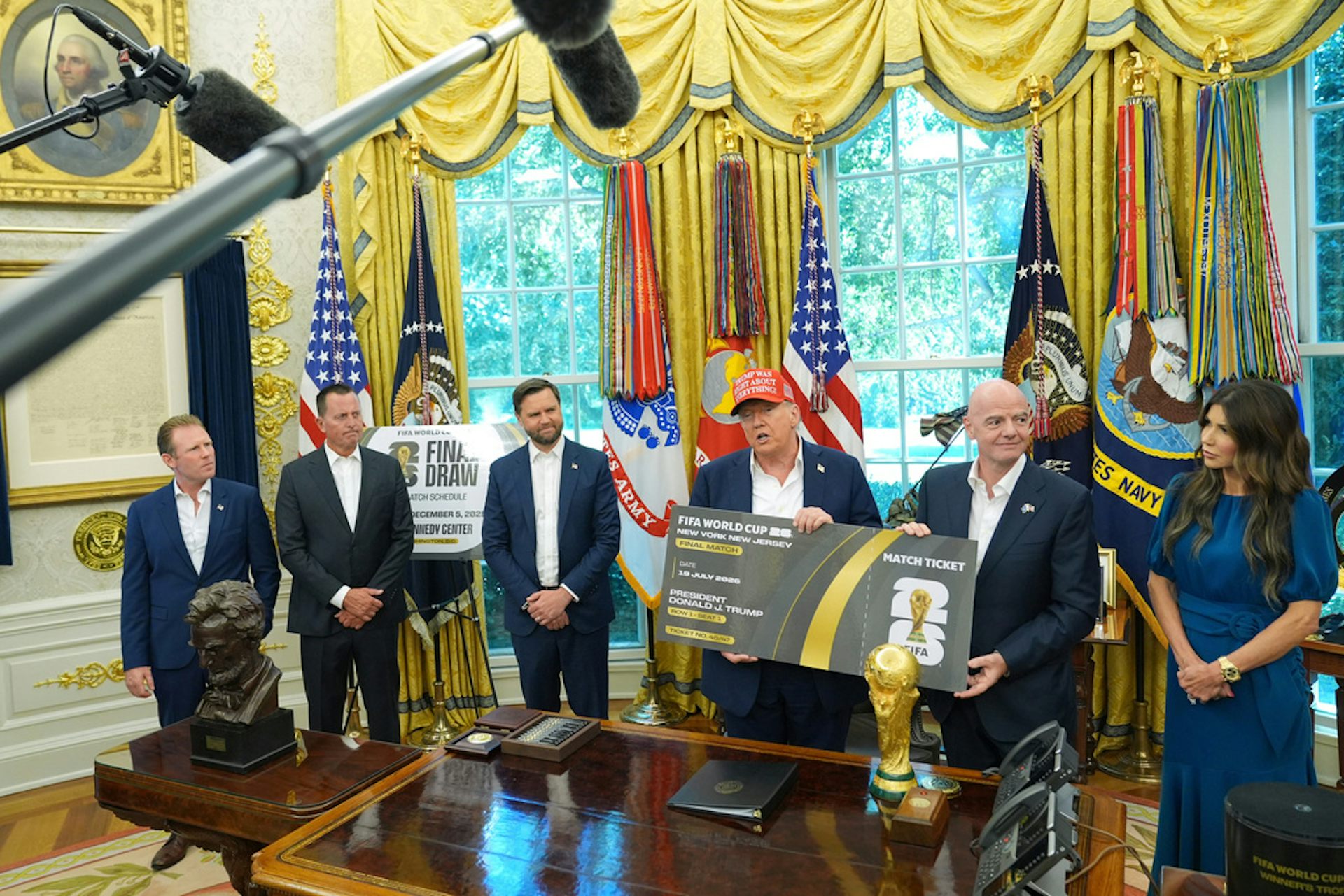 People in business attire stand around a desk during a press conference.