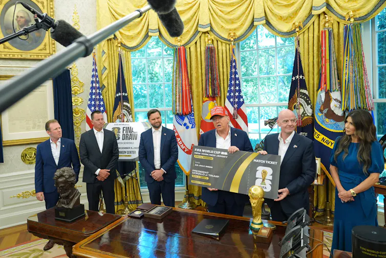 People in business attire stand around a desk during a press conference.