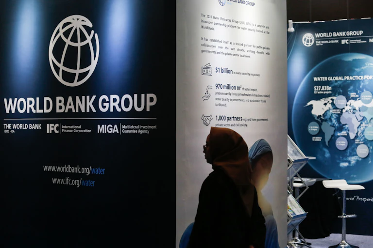 Person walking past a World Bank logo and information material on a wall