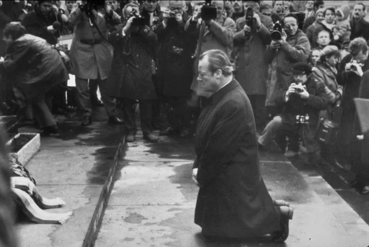 Fotografía en blanco y negro de un hombre arrodillado en la acera cerca del monumento.