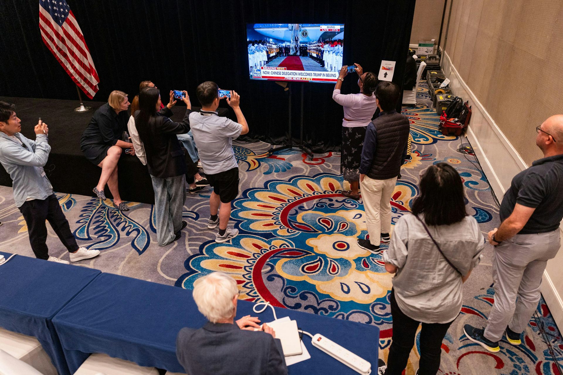 Journalists surround a television set which is showing US president DOnald Trump arriving in Beijing.