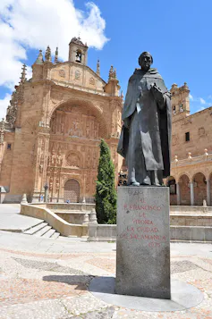 Estatua a un hombre religioso con un libro en la mano colocada delante de una iglesia.