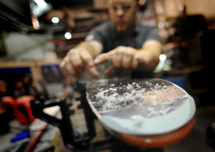 Curls of wax are visible at the end of a ski as a wax technician prepares skis for use.