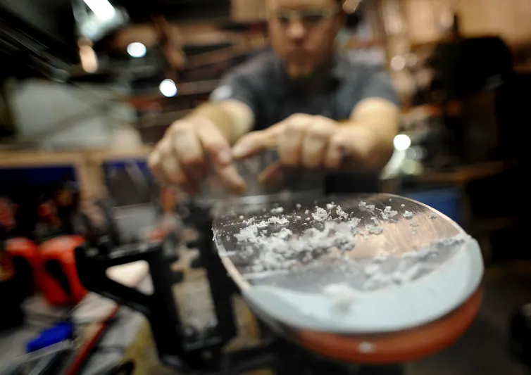 Curls of wax are visible at the end of a ski as a wax technician prepares skis for use.