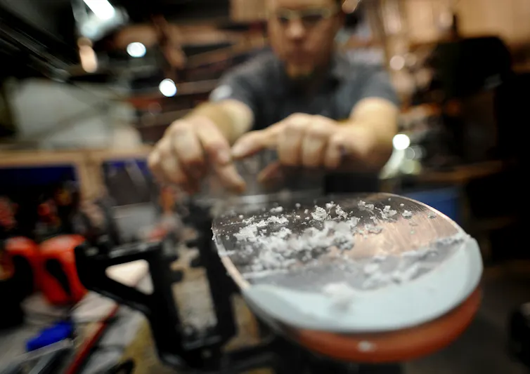 Curls of wax are visible at the end of a ski as a wax technician prepares skis for use.