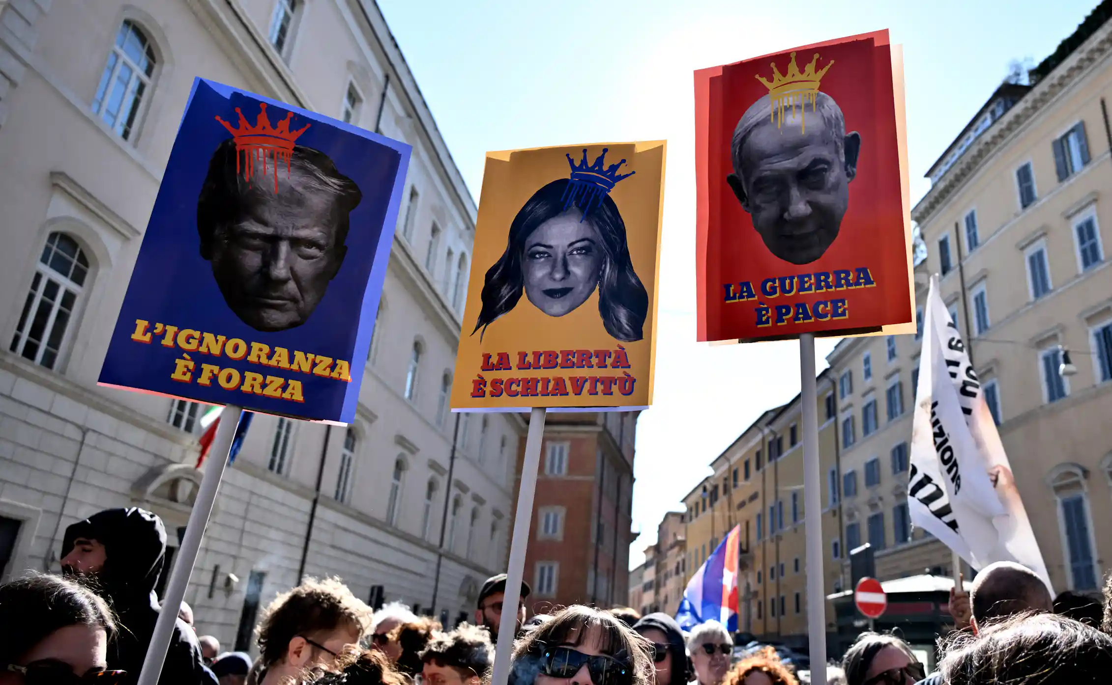 Protestors carry three posters depicting lawmakers with crowns on their heads.