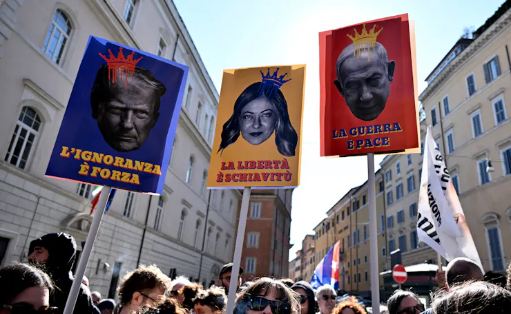 Protestors carry three posters depicting lawmakers with crowns on their heads.