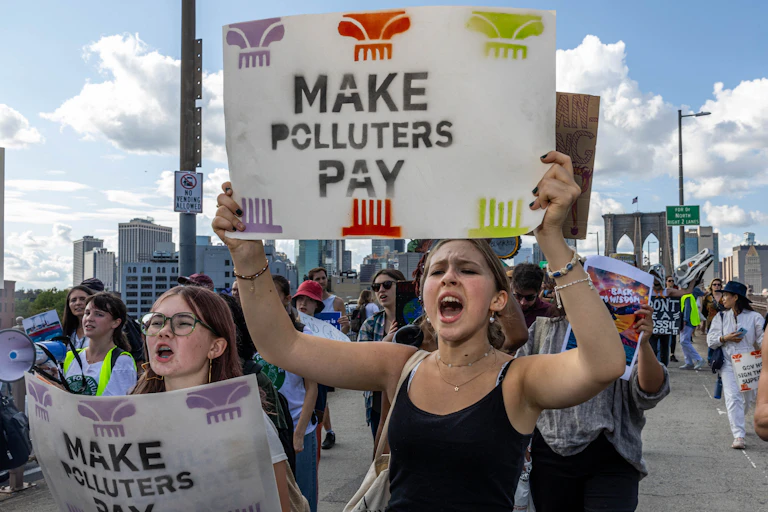 Demonstrators hold signs including one saying 'Make polluters pay.'