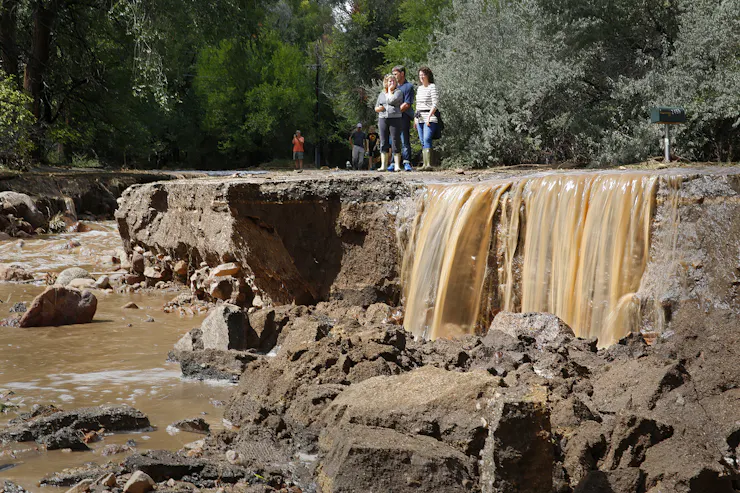 People stand on a road that has been eroded by water, which still runs nearby.
