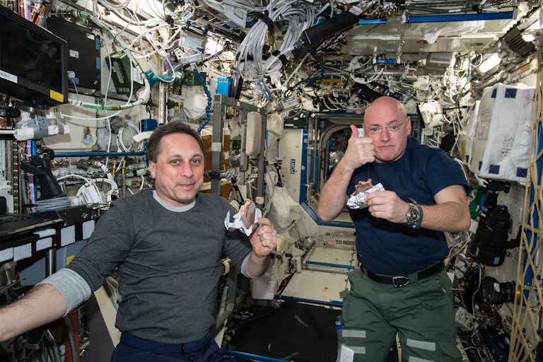 Two astronauts holding sandwiches. One is giving a thumbs up.