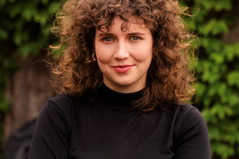 a curly haired woman in a black polo neck jumper