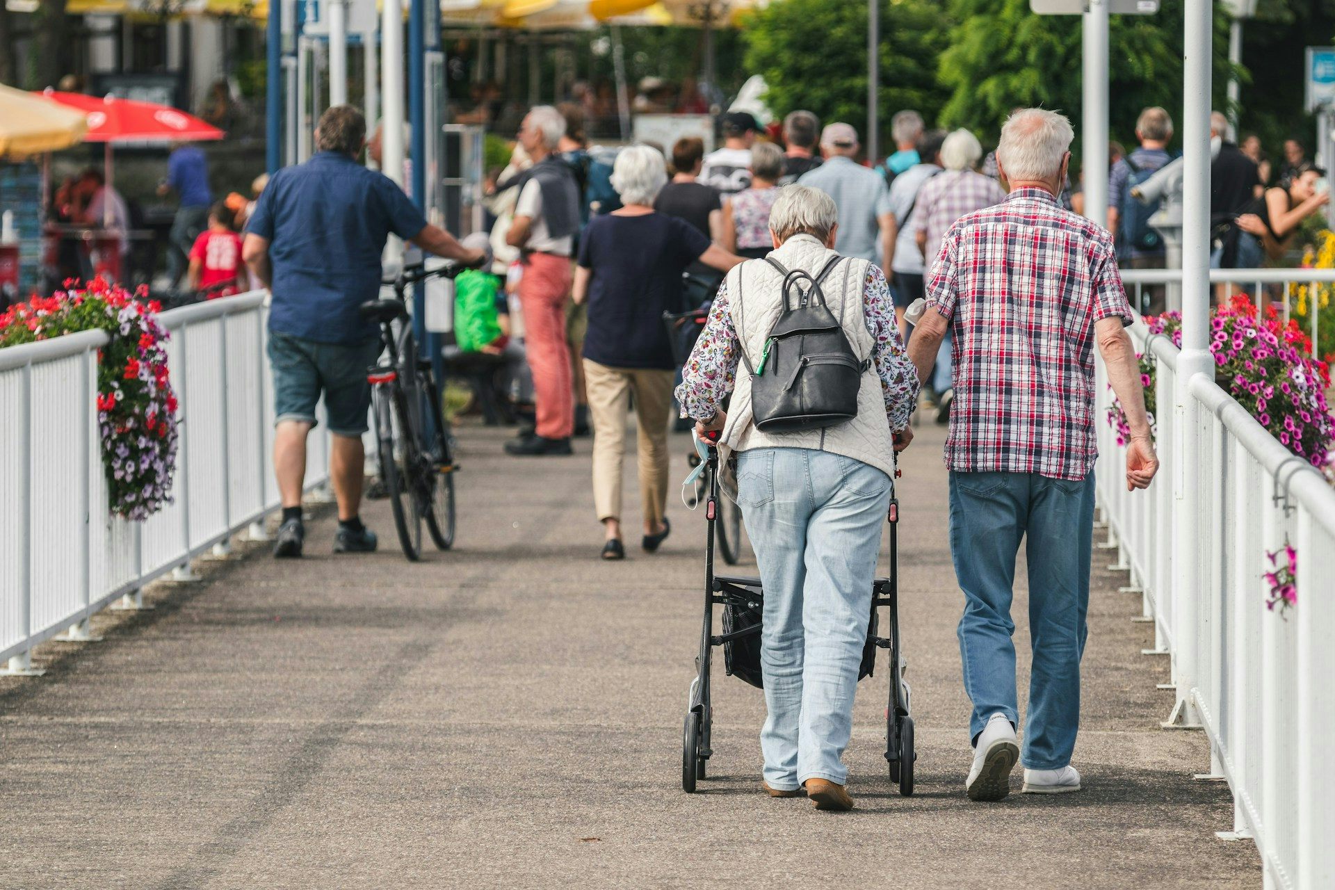 Elderly man walks arm-in-arm with an elderly woman using a walker.