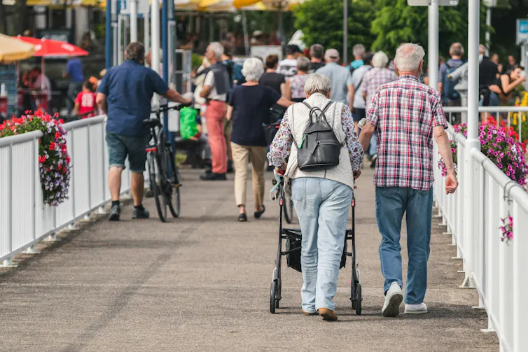 Un homme âgé marche bras dessus bras dessous avec une femme âgée qui utilise un déambulateur