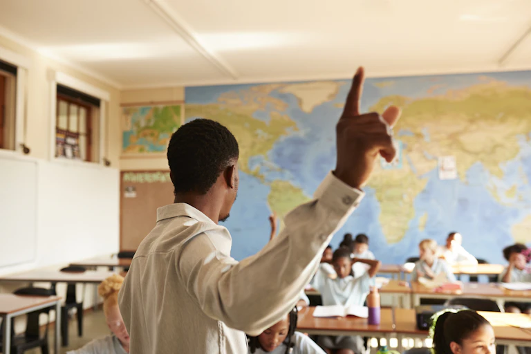 Man gesturing while standing in front of children at desks in classroom