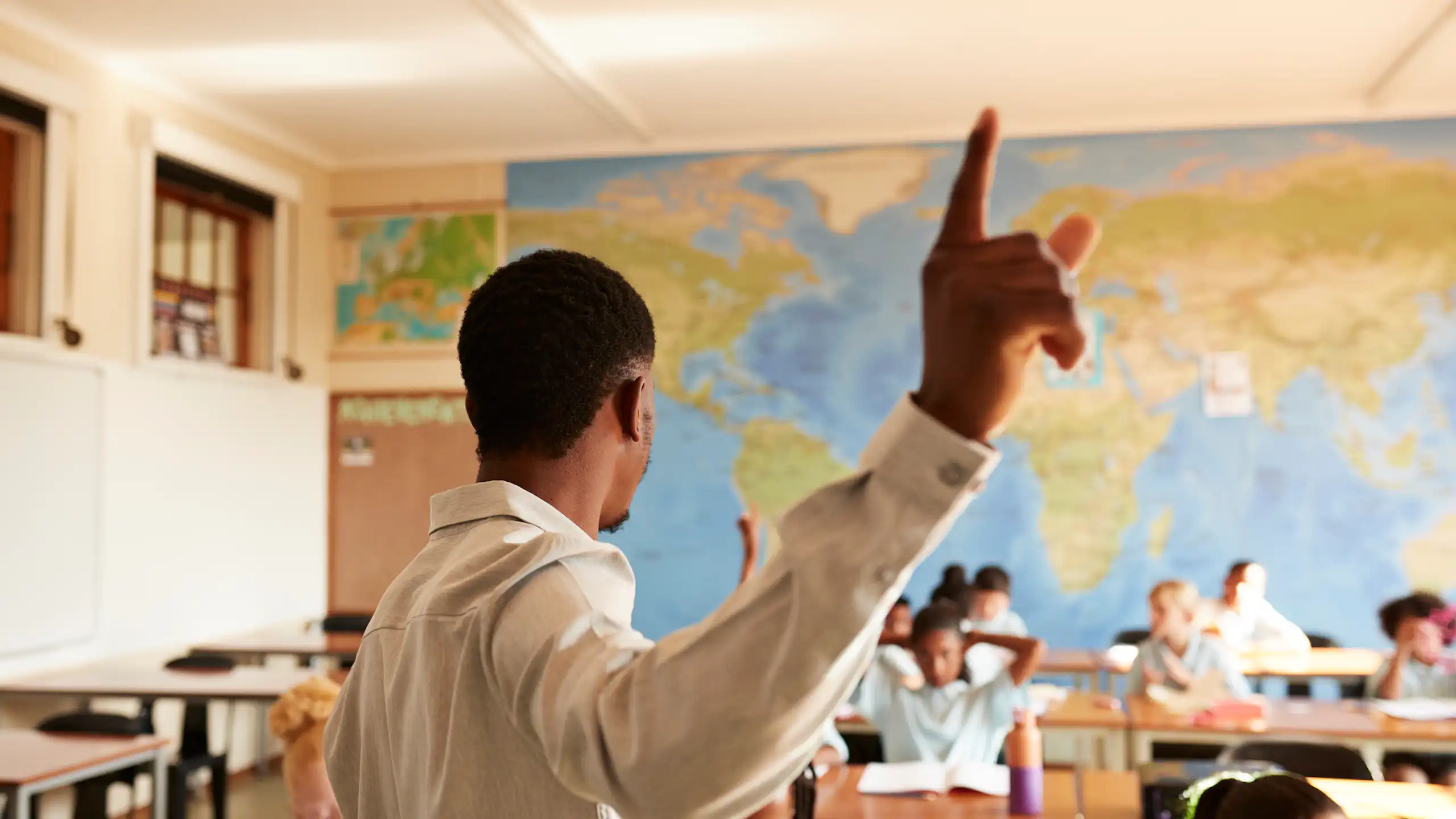 Man gesturing while standing in front of children at desks in classroom