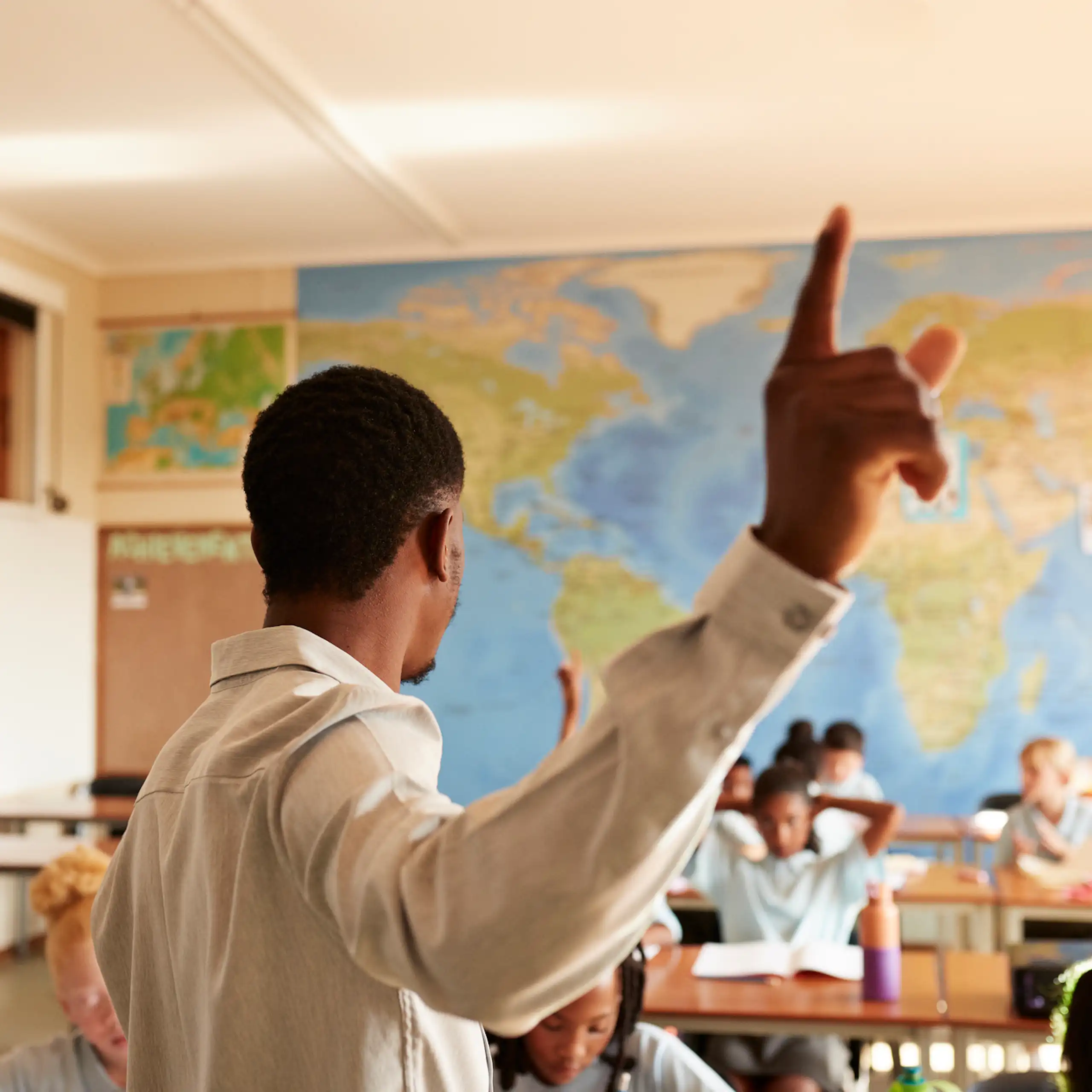Man gesturing while standing in front of children at desks in classroom