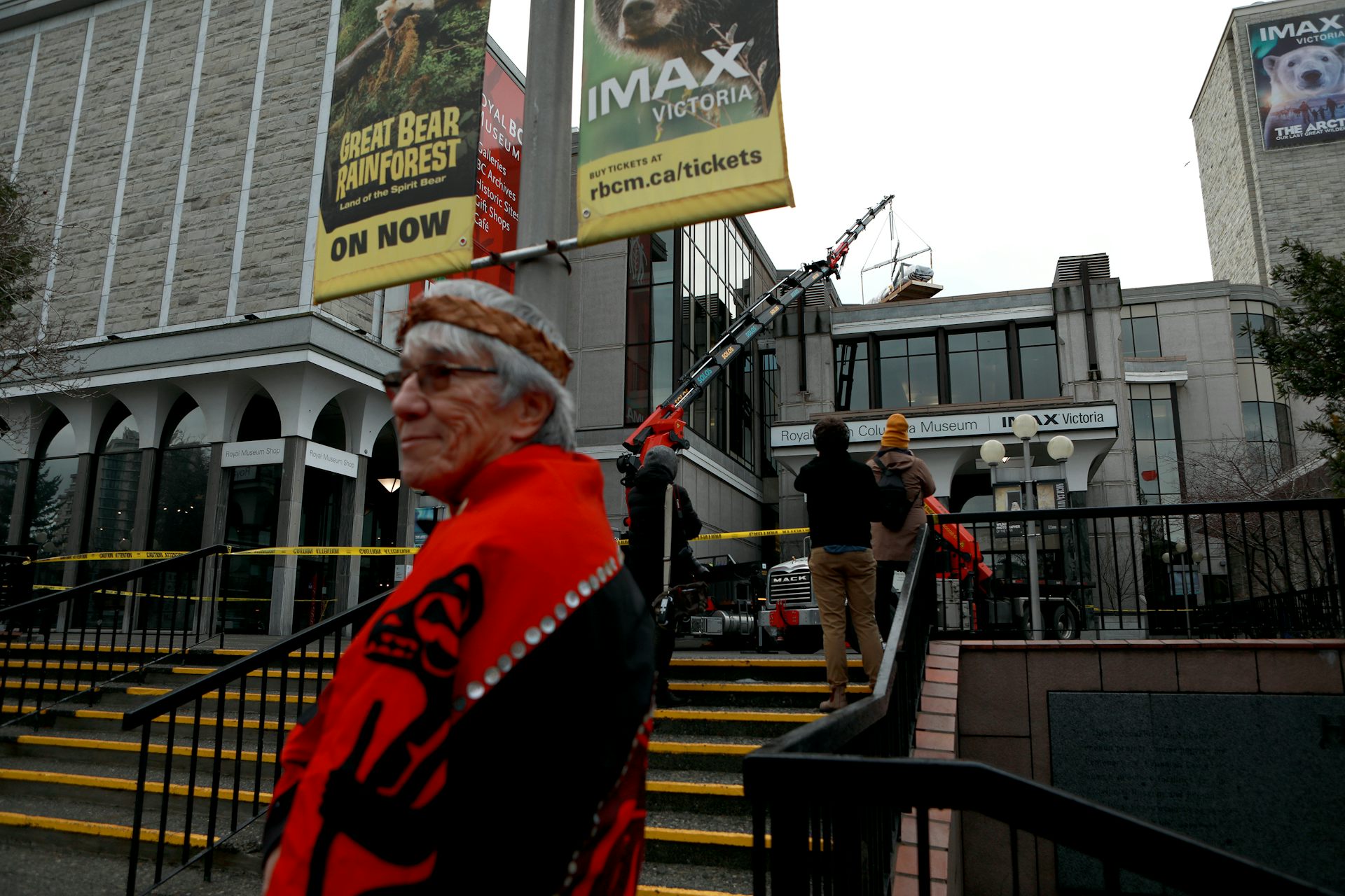 A person wrapped in a red and black blanket stands in sunglasses in front of a museum.