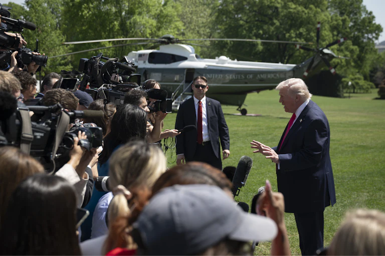 A man and a crowd of reporters outside with a helicopter in the background.