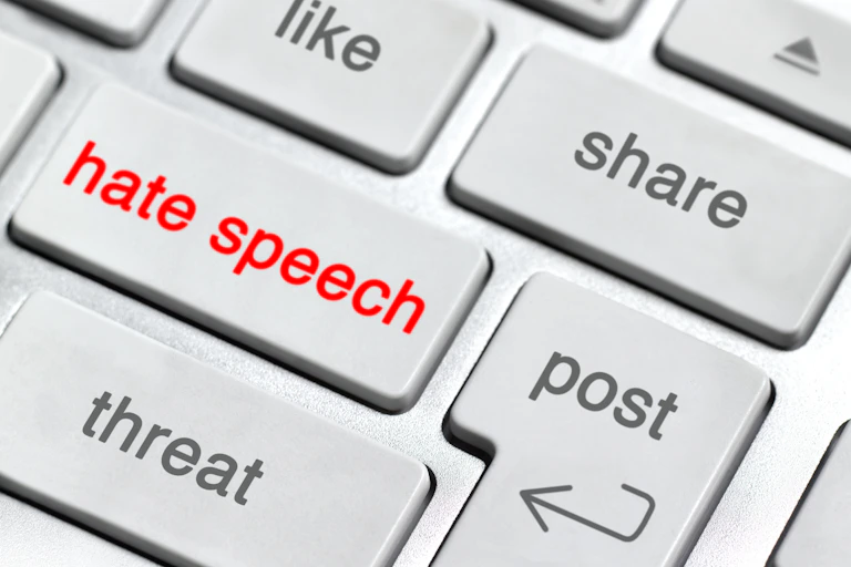 A section of a computer keyboard, with keys that say 'share,' 'post,' threat,' 'like' and 'hate speech,' which is in red font.
