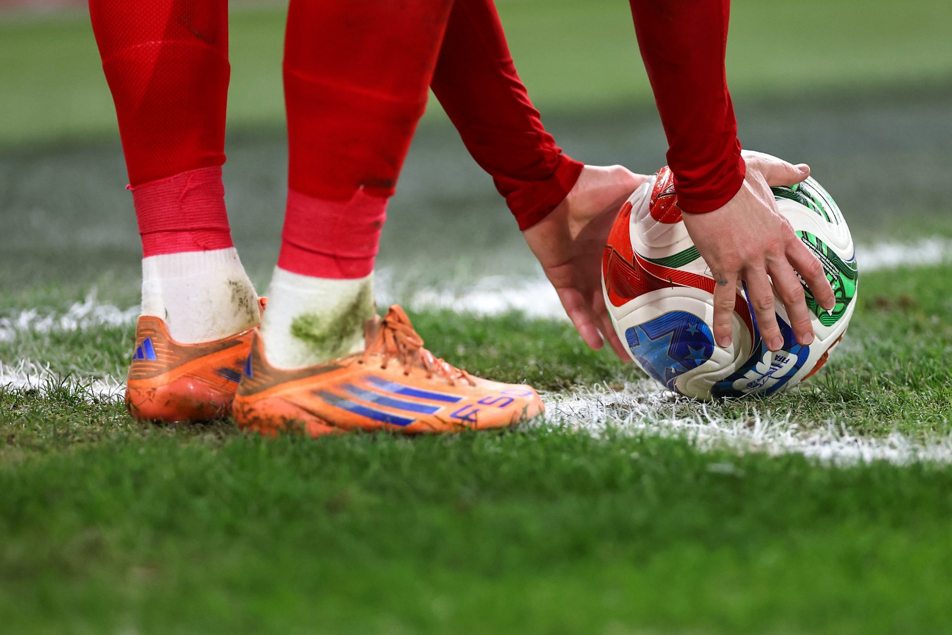 Um homem de meias vermelhas coloca uma bola no gramado.