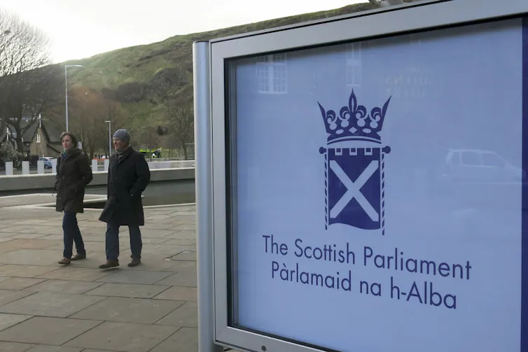 Two people walk past a billboard sign.