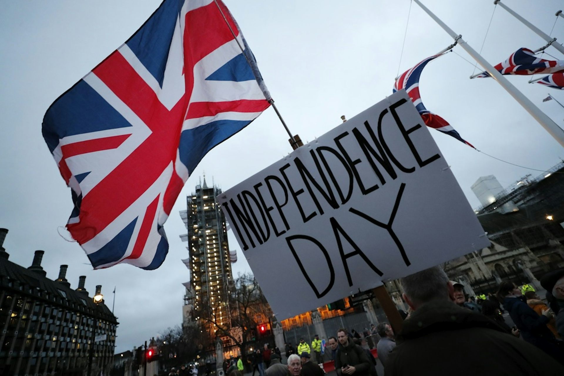 A protester holds a sign in front of a large flag.