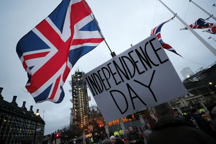 A protester holds a sign in front of a large flag.