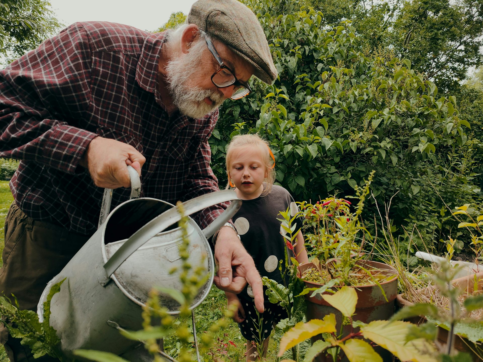 Un anciano riega el jardín y una joven observa a su lado.