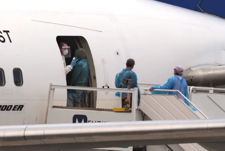A person boarding a plane accompanied by people wearing personal protective equipment