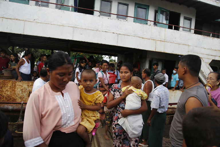 Two women holding babies among a group of people in a crowded street