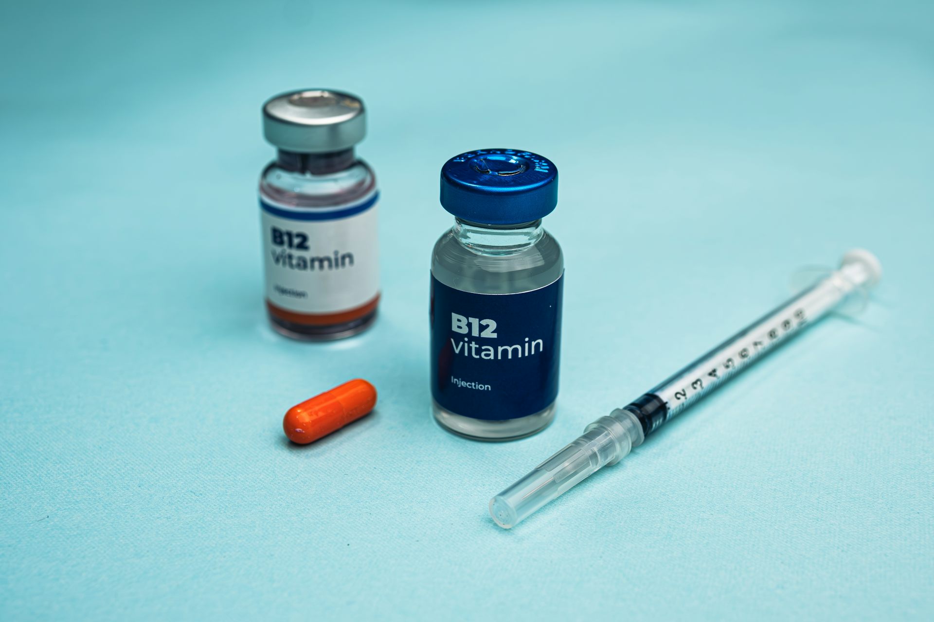 Dois frascos de vitamina B12 e uma seringa estão ao lado de uma cápsula laranja