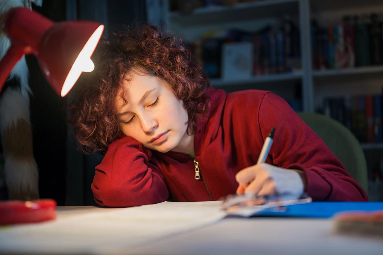 A young person works at a desk under a lamp.