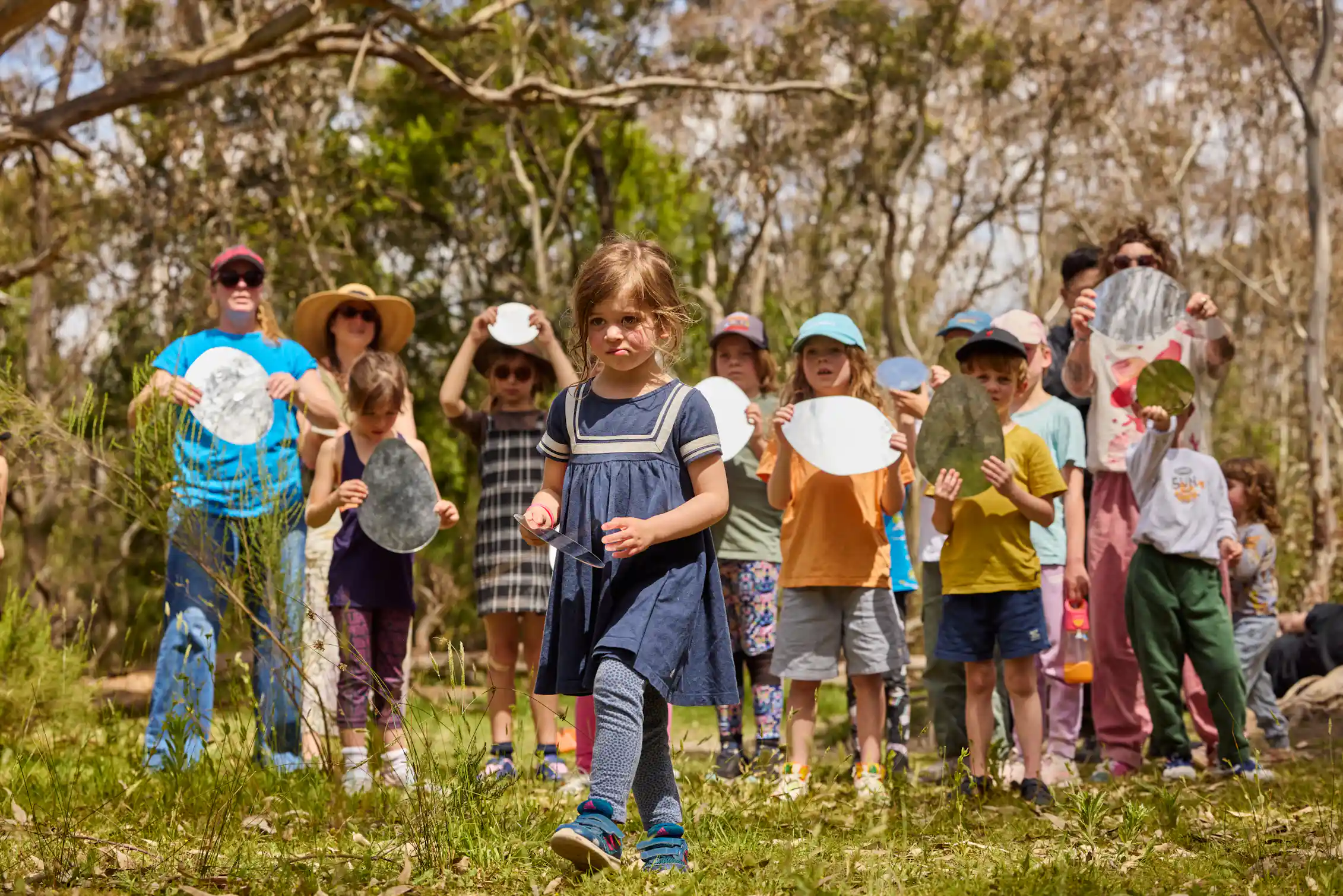A young girl walks ahead of a crowd of children with mirrors.