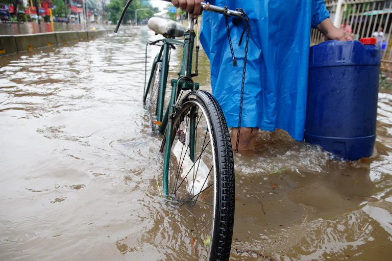 A person wearing a waterproof jacket wades a bike through a river.