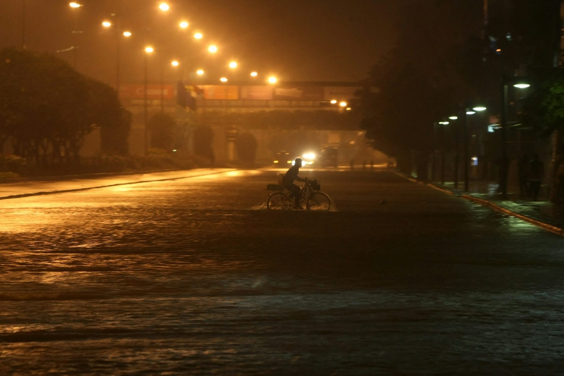A motorbike rides through a flooded street at night.